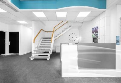 Reception area featuring a sleek grey desk, modern staircase, and blue ceiling accents.