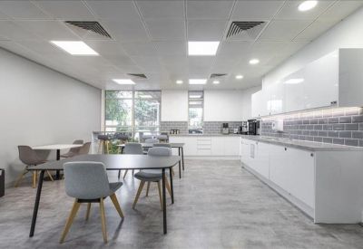 Communal kitchen and dining area with white cabinetry, grey tiling, and modern dining sets.