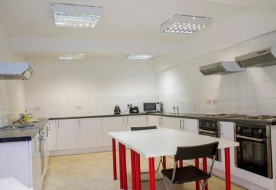 Bright communal kitchen and dining area with white cabinetry and a red-legged table.