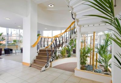 Bright lobby featuring a sweeping staircase with wooden handrails and indoor tropical plants.