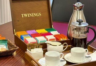 Wooden tea and coffee tray with a variety of Twinings tea bags, a silver carafe, and white cups.