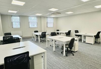Bright open-plan office with white desks, black chairs, and large windows providing natural light.