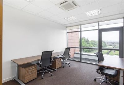 Bright private office with two wooden desks and large windows overlooking greenery.