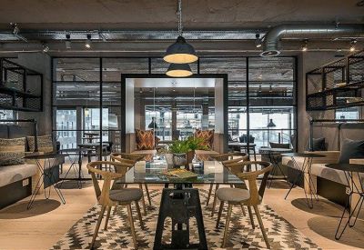 Spacious lounge area with wooden chairs, glass tables, and industrial piping.