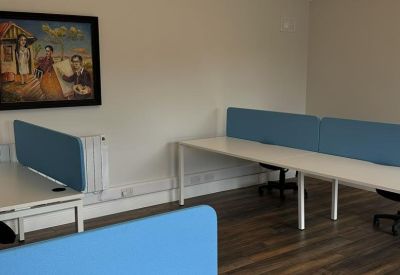 Close-up of a white office desk with a blue acoustic screen and hardwood floors.