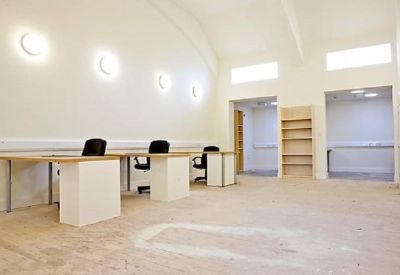 Open-plan workspace with multiple white desks, black chairs, and circular wall-mounted lights.