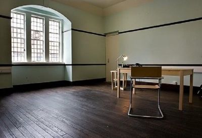 Private office featuring dark wood flooring, a simple desk, and a large arched window with natural light.