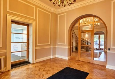 Grand entrance hall with polished parquet flooring and an ornate brass chandelier.