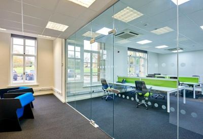 Modern glass-walled office space with bright desks and blue accent seating.