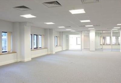 Spacious, open-plan office floor with white columns and bright square ceiling lights.