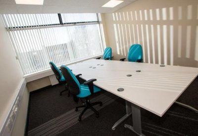 Sunlit meeting room featuring a white boardroom table and vibrant turquoise office chairs.
