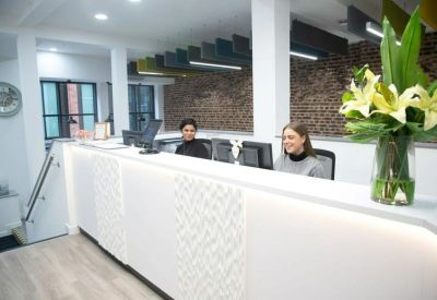 Modern white reception desk featuring a textured front panel, floral arrangement, and brick accent wall.