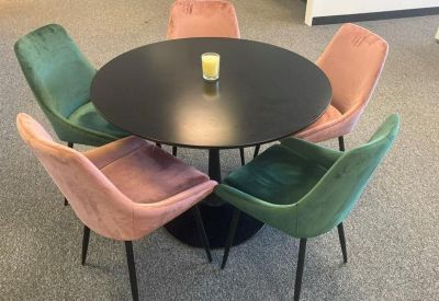 Modern breakout area featuring a round table and velvet chairs in pink and green.