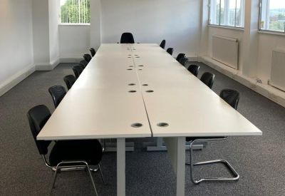 Spacious boardroom with a long white conference table and black office chairs.
