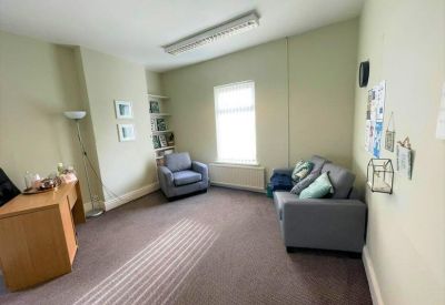 Spacious private office with a grey sofa, armchair, and wooden desk.