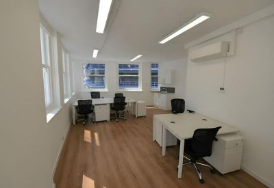 Modern open-plan office suite with white desks, black chairs, and light wood flooring.