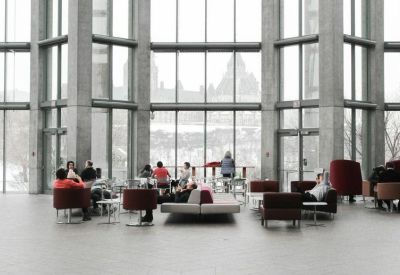 Large sunlit lobby with high glass walls and comfortable red and grey lounge seating.