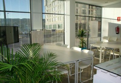 Bright glass-walled meeting room with white tables and green plants.