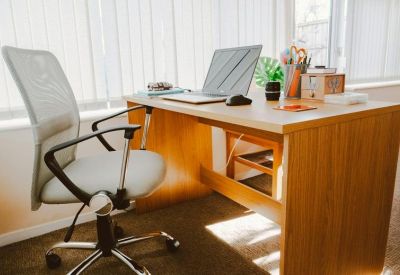 Private wooden desk setup with an ergonomic chair and laptop by a window.