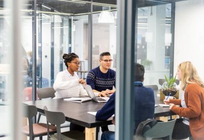 Internal meeting room with a group of people discussing work around a dark table.