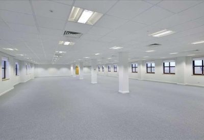 Spacious, bright open-plan office floor with white pillars and rows of windows.