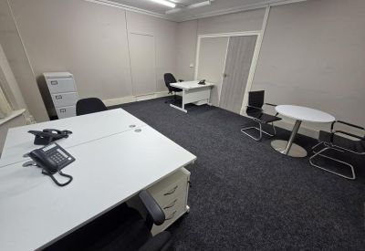 Spacious office suite with multiple white desks and dark grey carpeting.