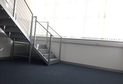 Bright office space featuring a metal staircase and large windows with blinds.