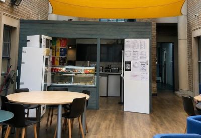 Indoor breakout area with a yellow sun shade, round wooden tables, and a snack bar.