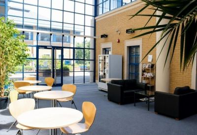 Bright glass-walled lobby with cafe seating, black leather sofas, and large leafy plants.