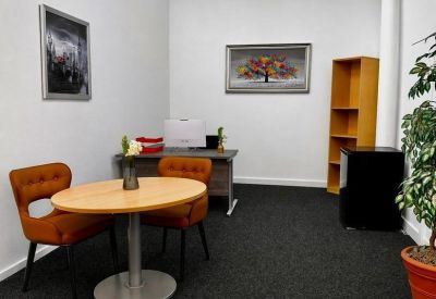 Small breakout area with two orange chairs, a round table, and a colorful tree painting.