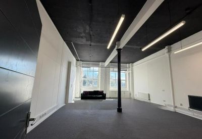 Large open-plan office featuring high black ceilings, industrial pillars, and linear LED lighting.