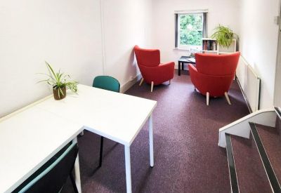 Breakout space with a desk and vibrant red armchairs on purple carpeting.