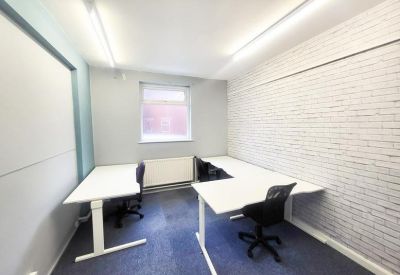 Bright private office with white desks and a white brick feature wall.