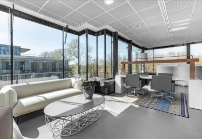 Sunlit breakout lounge with a cream sofa, oval coffee table, and wrap-around windows.