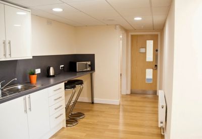 Modern communal kitchen with white cabinetry, wood flooring, and a breakfast bar with stools.