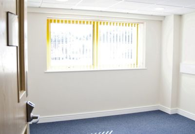Internal office suite with blue carpeting, a large window with yellow blinds, and overhead lighting.