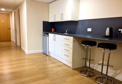Bright communal kitchenette area featuring integrated appliances and a long grey breakfast bar.