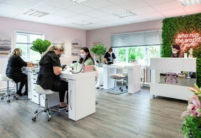 Bright beauty salon space with white manicure stations and a green foliage feature wall.