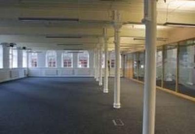 Spacious open-plan office with white industrial pillars and dark blue carpeting.