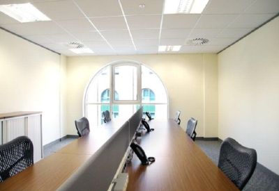Bright private office featuring long wooden desks and an arched window.