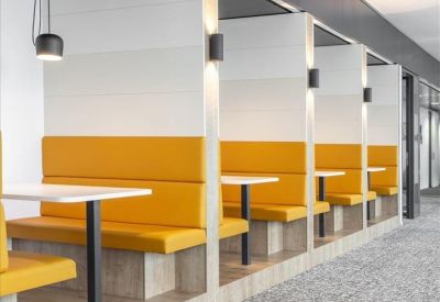 Modern communal breakout area featuring vibrant yellow booths and warm wood accents.