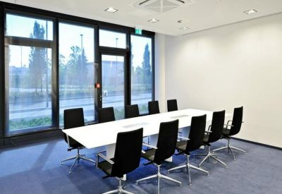 Bright conference room with a long white table, black chairs, and floor-to-ceiling windows.