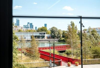 View through a window of a modern red bridge and landscaped park in a city setting.