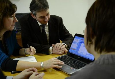 Three professionals collaborating around a laptop at a wooden desk.