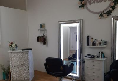 Bright salon workspace with a large illuminated mirror, white dresser, and floral wall decor.