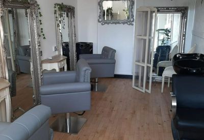 Hairdressing studio featuring ornate silver mirrors and grey styling chairs on wood-effect flooring.