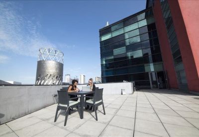 Outdoor roof terrace with seating overlooking urban architecture.