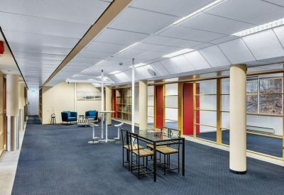 Large open corridor with a dining table and glass-partitioned offices.