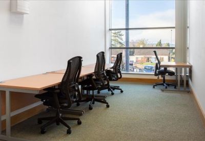 Long workstation with ergonomic black mesh chairs and large windows.