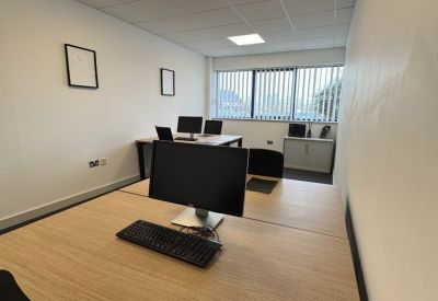 Office workspace with multiple desks, computer monitors, and vertical window blinds.